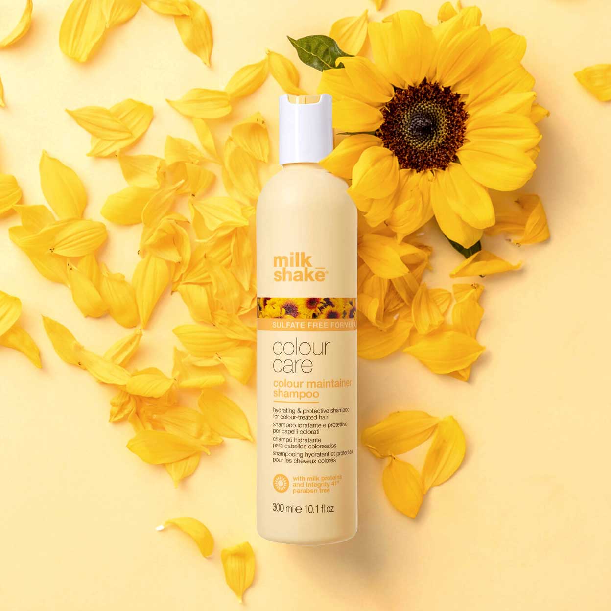 Milk Shake Sulfate-Free Colour Care Shampoo, 300 ml bottle, placed on a background of yellow sunflower petals. The bottle is beige with a sunflower design near the top and a white cap.
