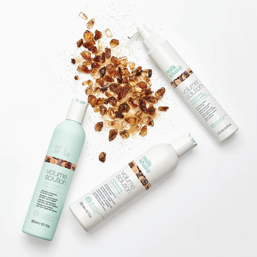 Milk_Shake Volume Solution haircare product group including shampoo and styling spray, displayed with a background of crystal-like granules.