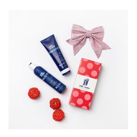 Milk_shake Cold Brunette Duo Set including two blue bottles, decorative red balls, and a pink glittery bow, alongside a red polka-dotted gift box.
